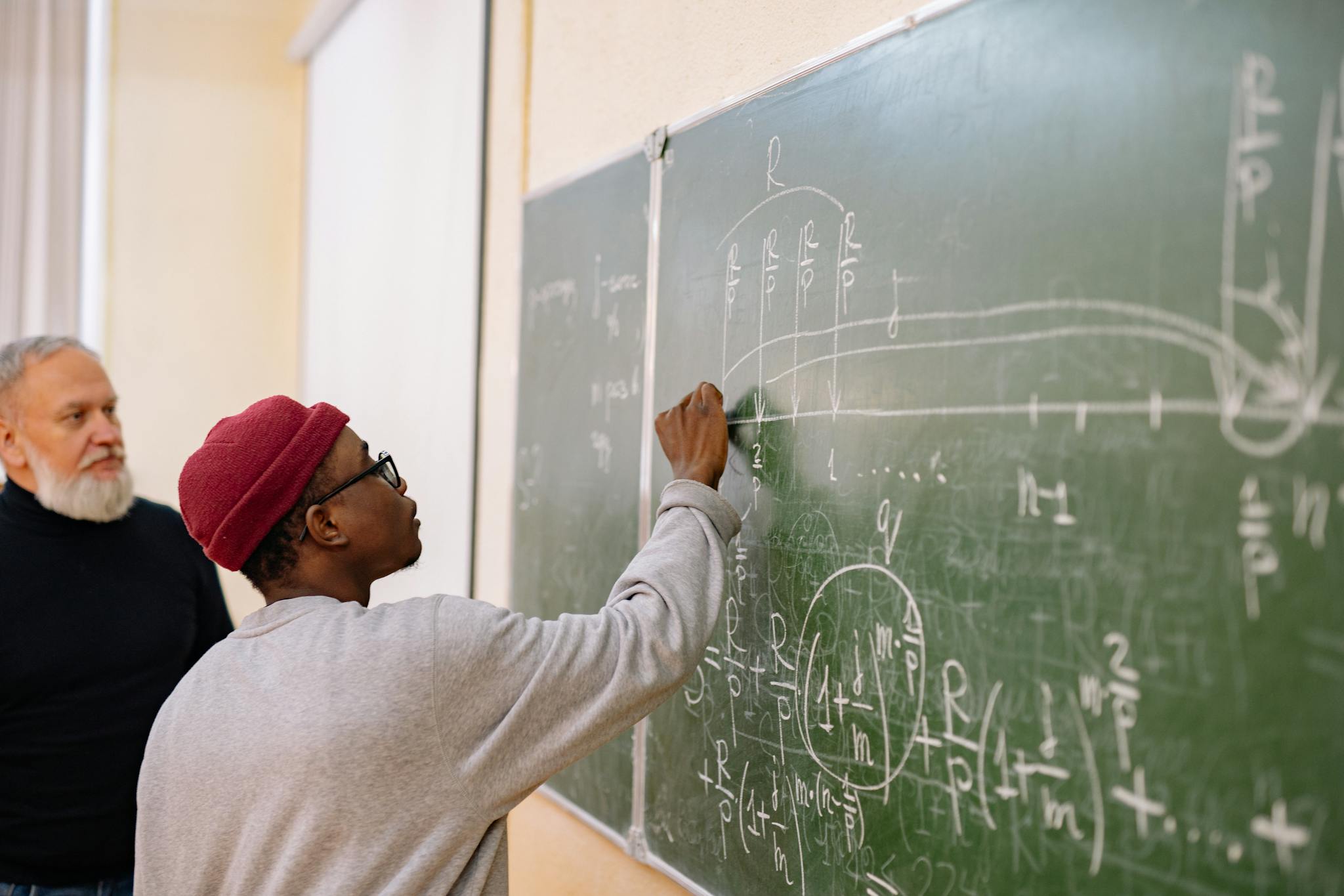 A student writes complex mathematical equations on a chalkboard during a university lecture.