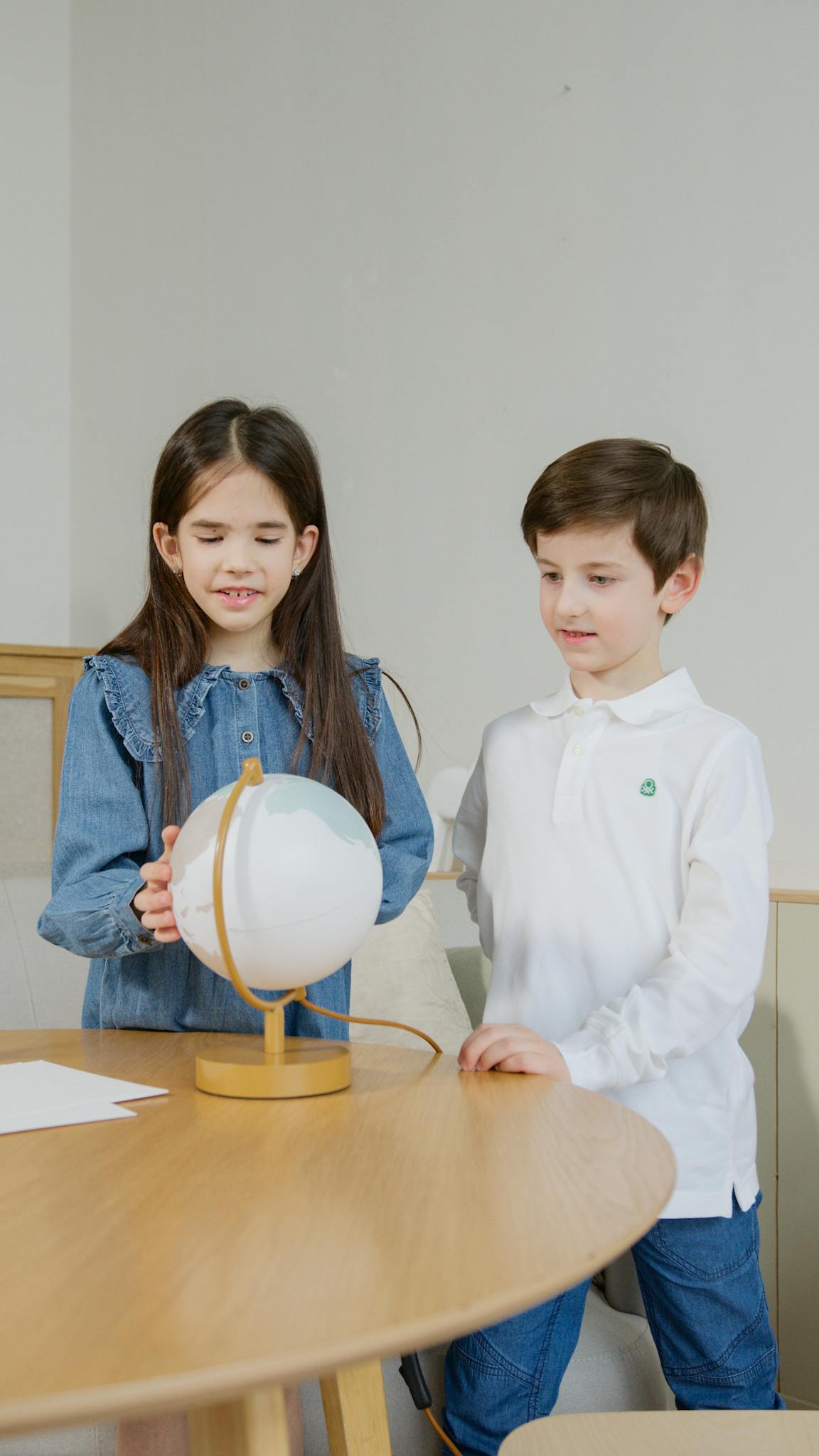 Two children engage with a globe, learning geography in a classroom.